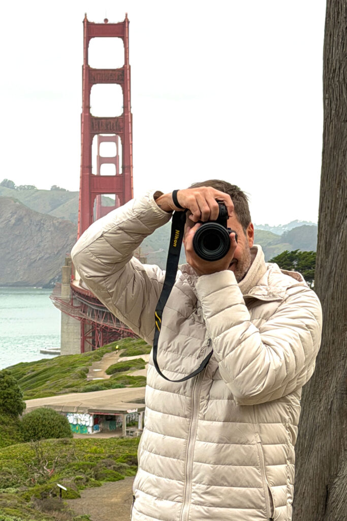 Portrait of Rodrigo Cavassoni, food photographer in San Francisco, holding his camera in front of the Golden Gate Bridge